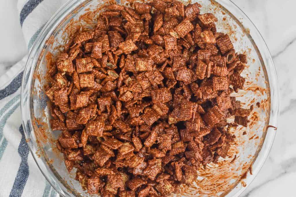 overhead view of a glass mixing bowl that is full of Chex cereal that has been coated in melted chocolate/peanut butter/butter to make muddy buddies