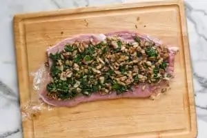 a flattened pork loin on a cutting board that is covered in spinach and mushrooms filling
