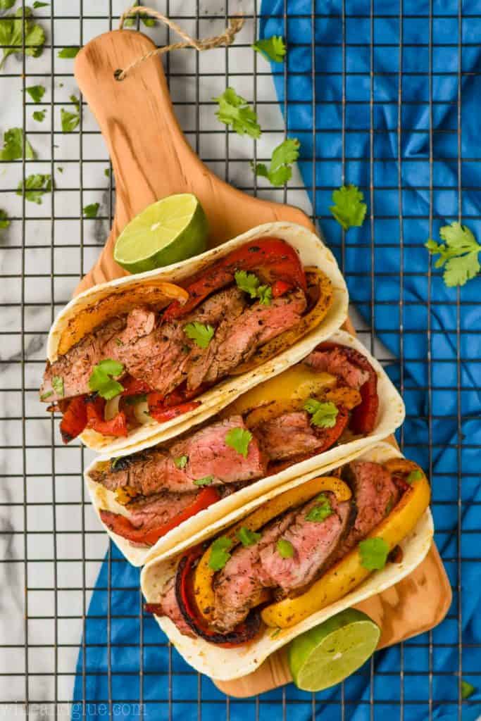 overhead view of three steak fajitas on a small wood cutting board on a wire rack, garnished with fresh cilantro