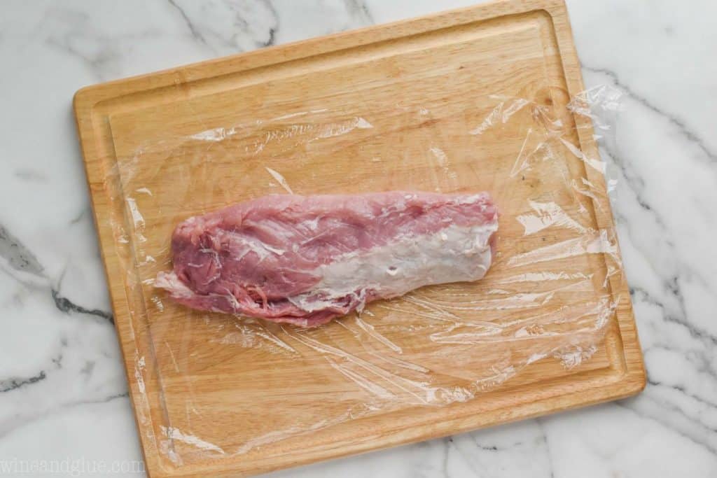 a pork loin that has been trimmed of excess fat and is on a sheet of Saran Wrap on a cutting board