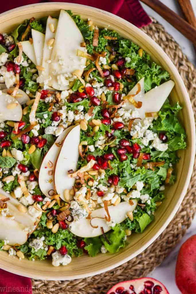 overhead view of a bowl of kale, pomegranate seeds, blue cheese, pine nuts, and pear slices for a winter kale salad