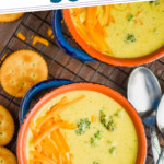 pinterest graphic of overhead view of a broccoli cheddar soup recipe in two small blue soup bowls on a wire cooling rack, with round orange crackers next to it and two spoons on the side, says "the best broccoli cheddar soup simplejoy.com"