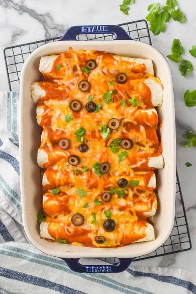 overhead of beef enchilada recipe in a ceramic baking dish with blue handles sitting on a wire cooling rack with cilantro around it on a marble counter top