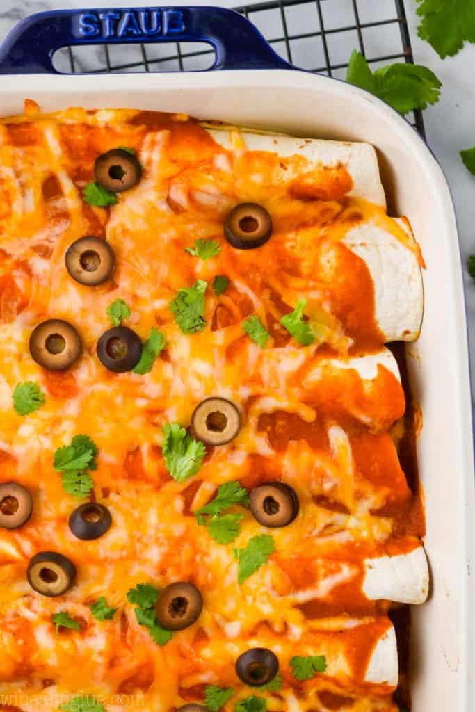 overhead of beef enchiladas in a ceramic baking dish, garnished with black olives and cilantro