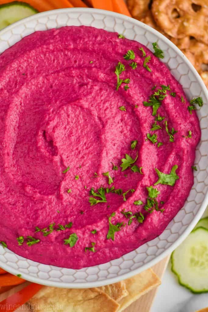 overhead view of a white bowl full of bright pink beet hummus garnished with fresh parsley