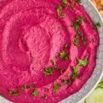overhead view of a white bowl full of bright pink beet hummus garnished with fresh parsley