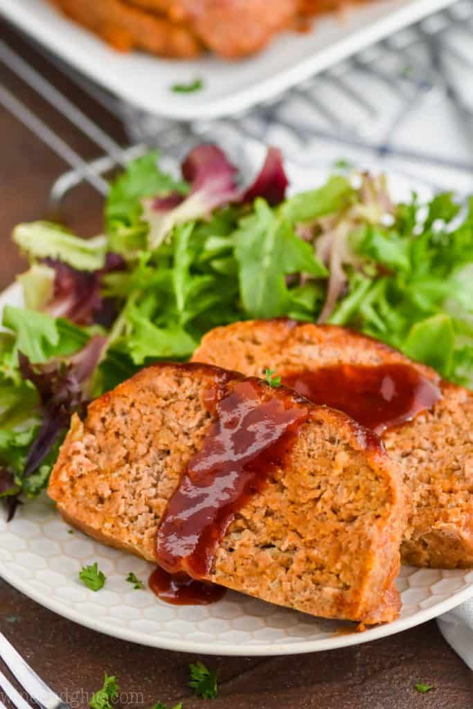 two pieces of turkey meatloaf on a white plate with salad, they have been topped with more bbq sauce