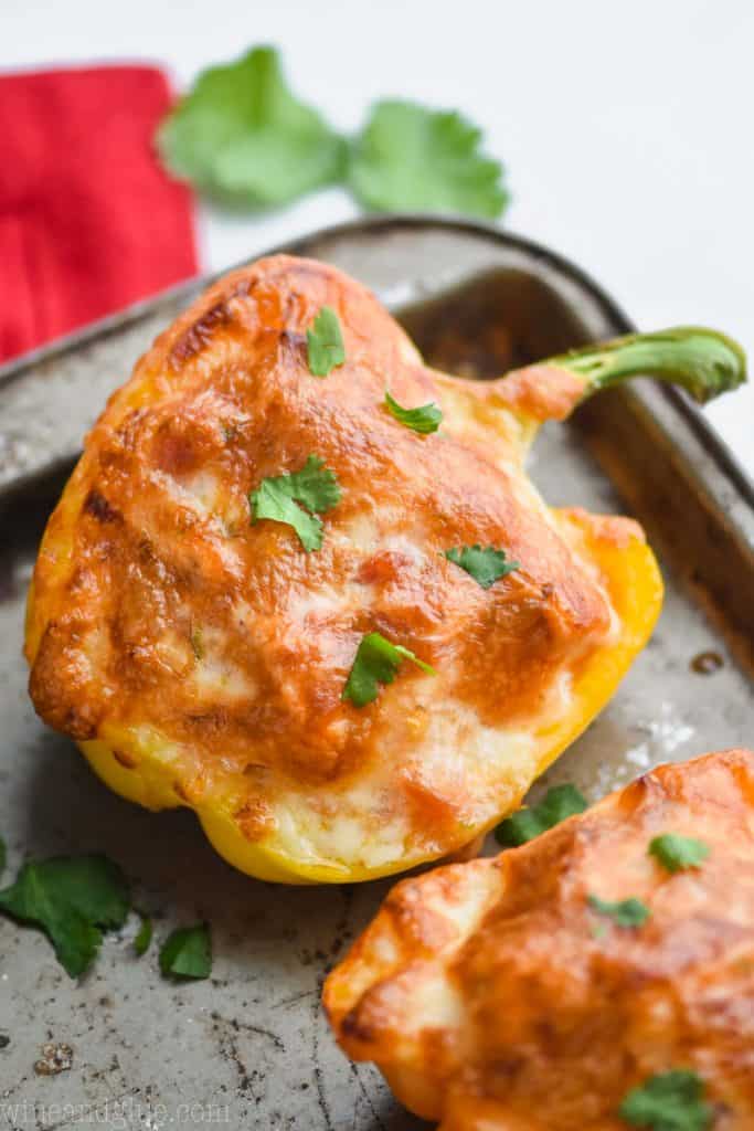 a half yellow bell pepper that is a chicken fajita stuffed pepper topped with bubbly brown cheese on an old baking sheet and garnished with cilantro