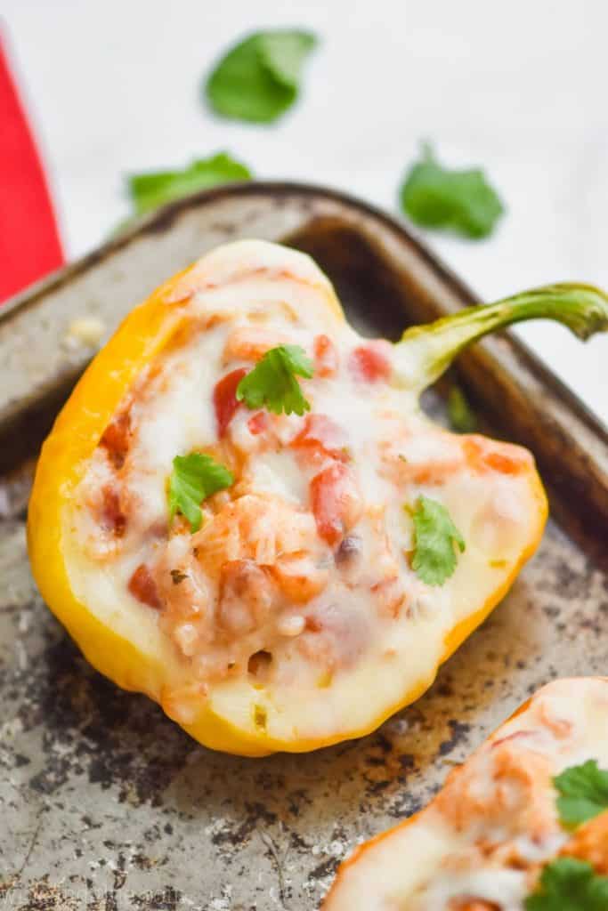 a yellow bell pepper stuffed with a chicken and rice mixture and topped with white melted cheese, on an old tray and garnished with cilantro