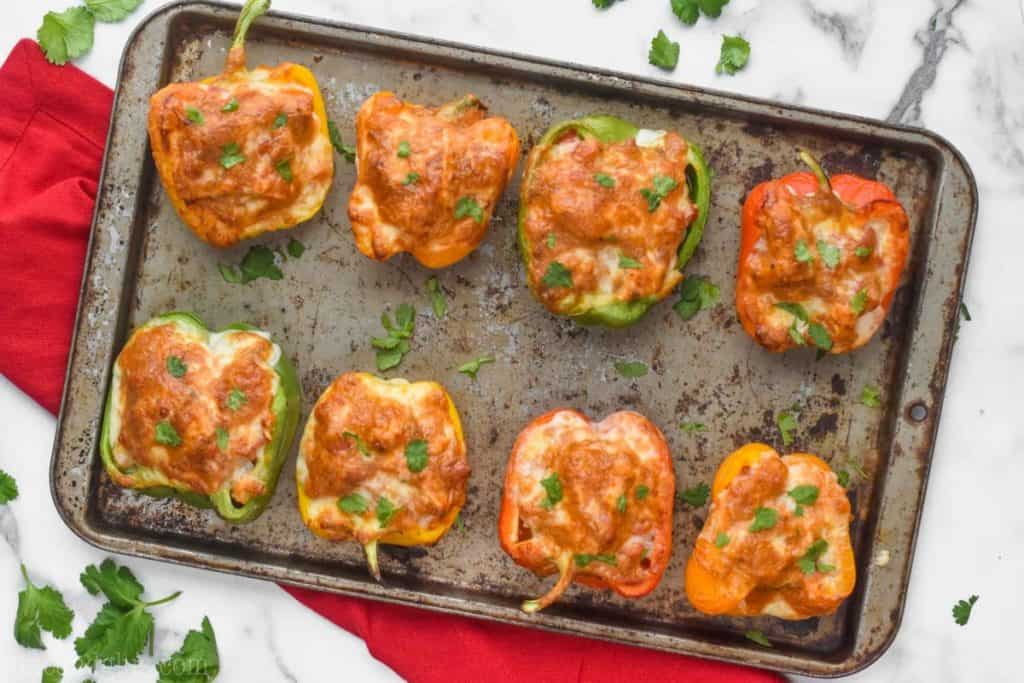 overhead view of 8 bell pepper halves that are chicken stuffed peppers, topped with brown melted cheese on an old tray and garnished with cilantro