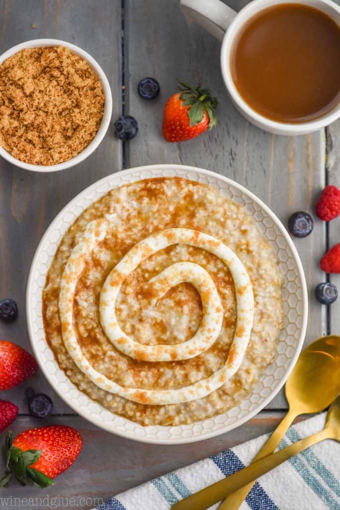 overhead view of cinnamon roll steel cut oats that have a swirl of frosting and brown sugar on top, lots of berries surrounding the bowl