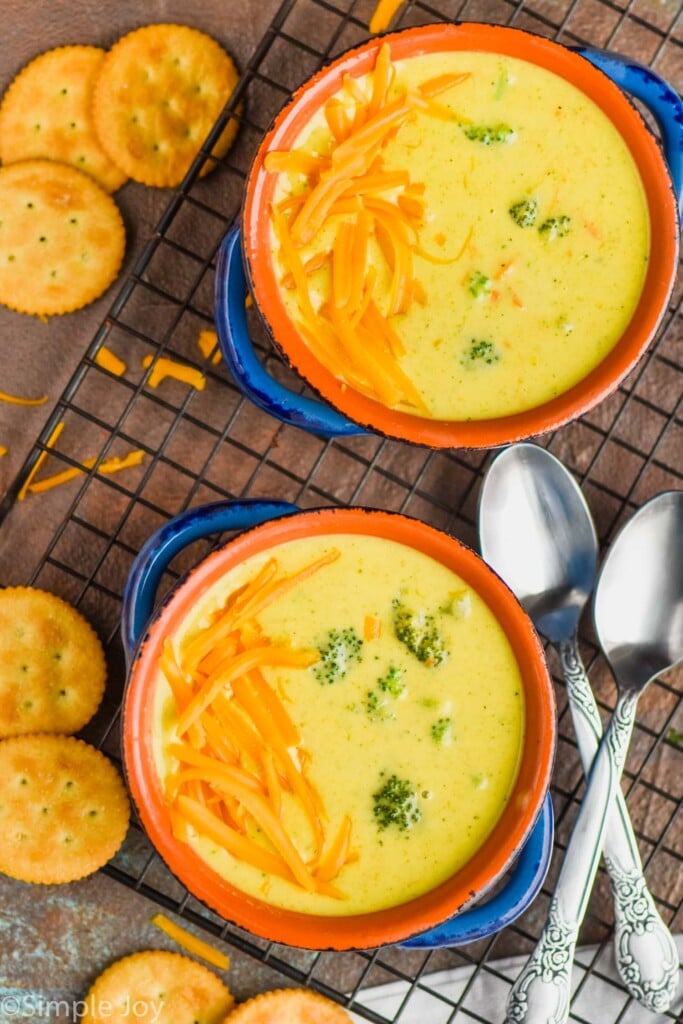 An overhead photo of two bowls of Broccoli Cheddar Soup with cheddar cheese sprinkled on one side and Ritz Crackers next to the bowl