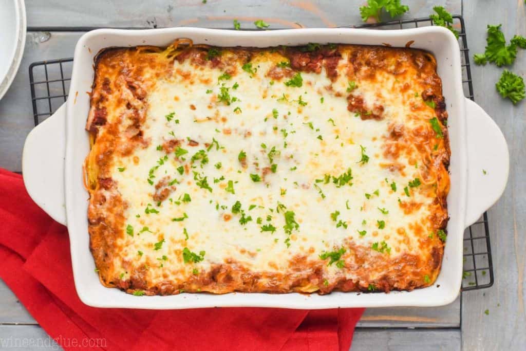 overhead view of a ceramic baking dish full of cheesy baked spaghetti topped with fresh parsley