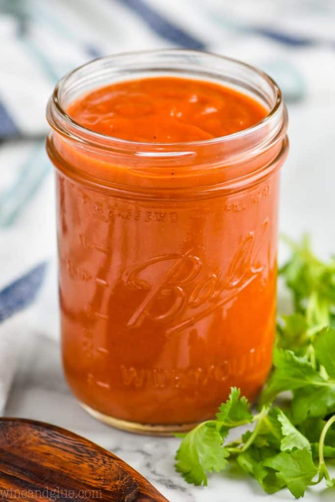 glass mason jar of enchilada sauce with cilantro next to it