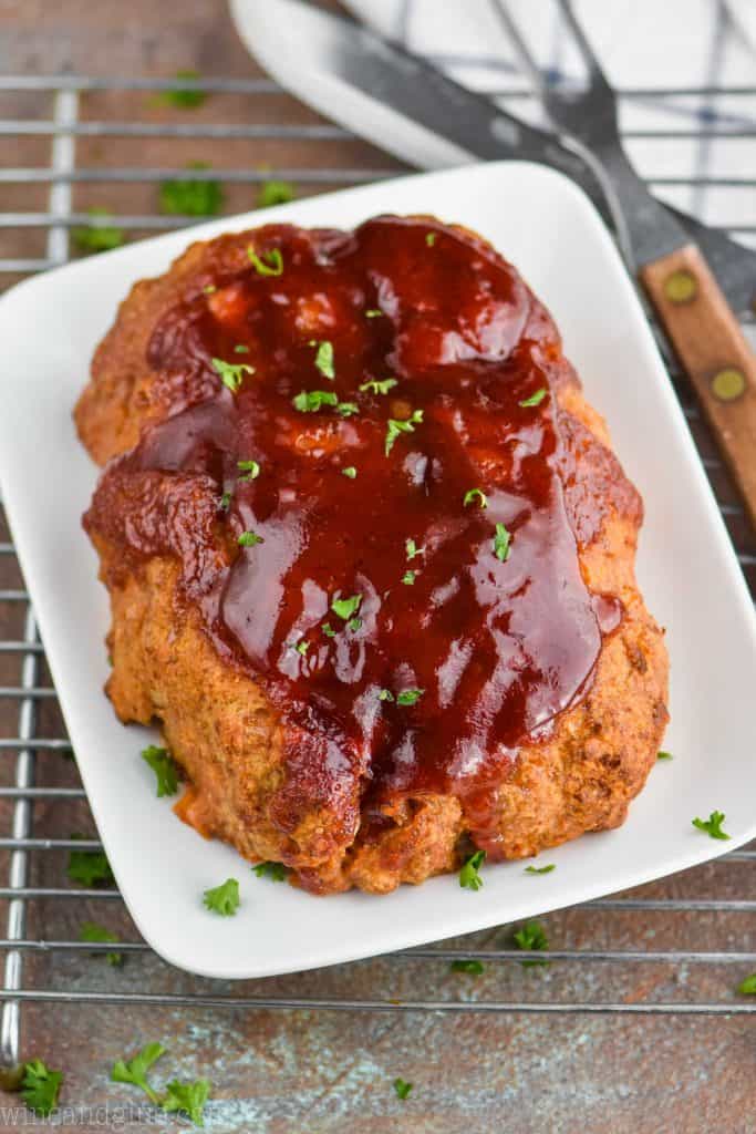 a whole healthy turkey meatloaf that is sitting on a white plate and on top of a wire rack, it is topped with bbq sauce and parsley