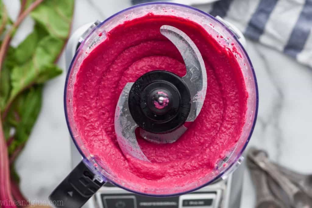 overhead view of a food processor that has processed beet hummus and it is smooth and bright pink