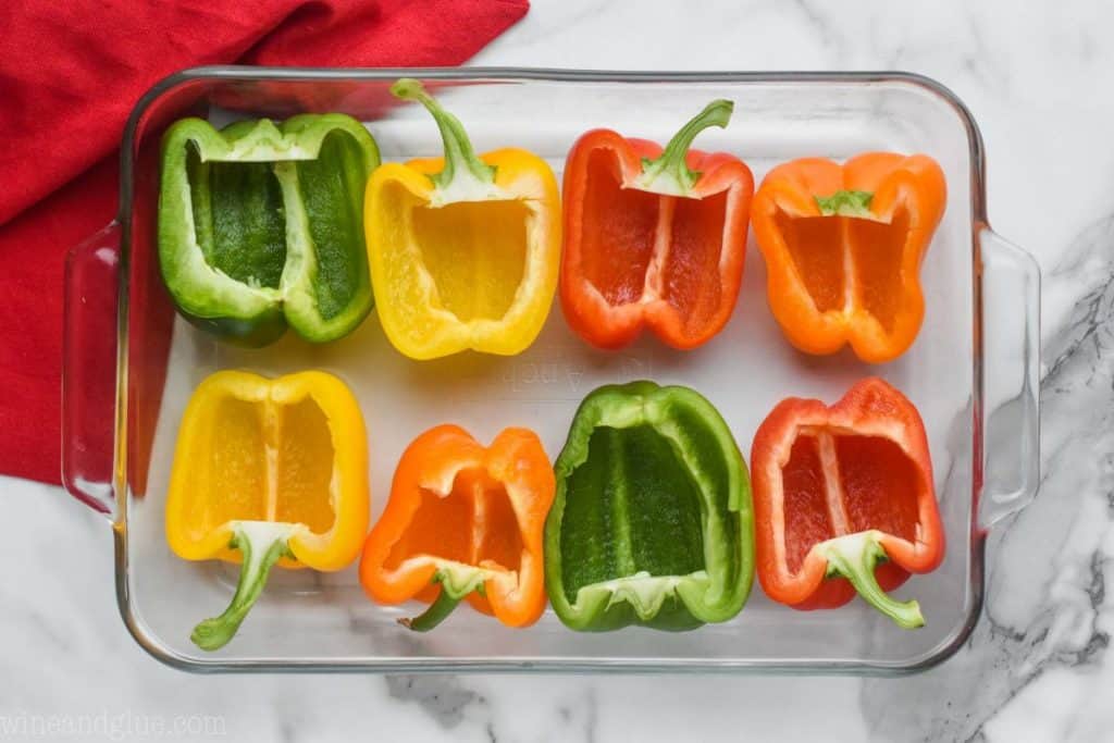 overhead view of a glass 9 by 13 baking dish with 8 half bell peppers that have had their seeds removed and are waiting to be pre baked