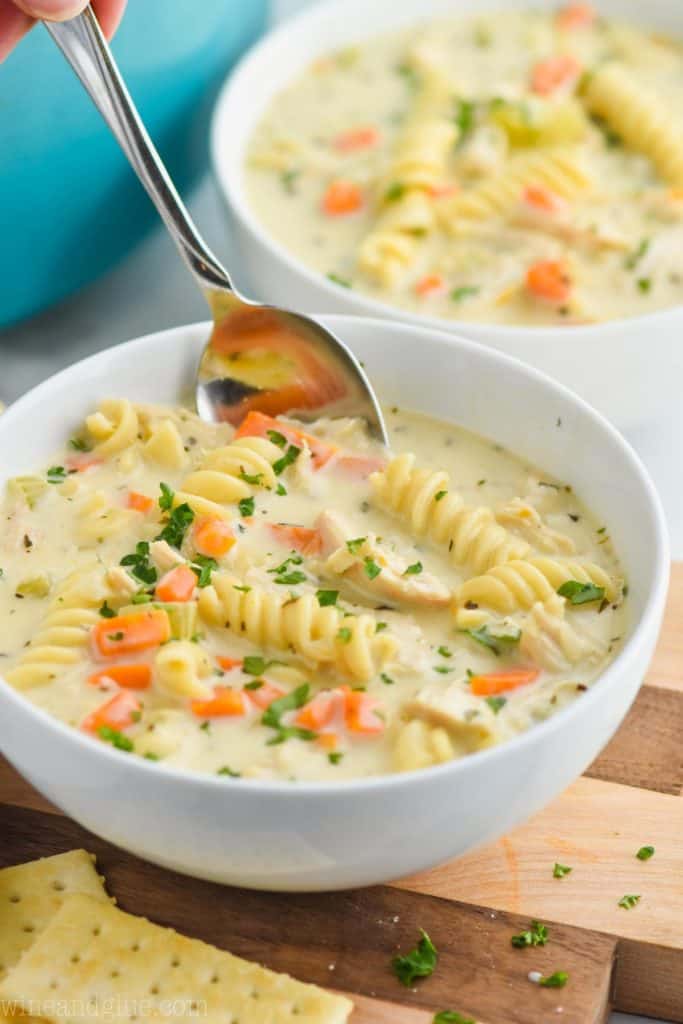 a white bowl full of the best creamy chicken noodle soup recipe with a spoon dipping in 