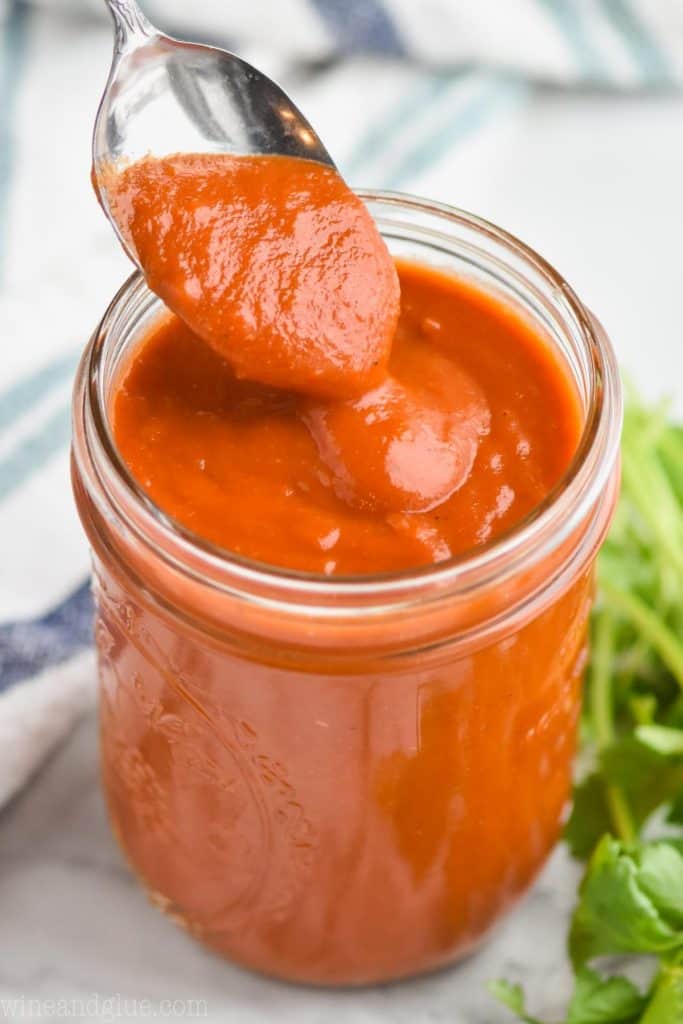 a spoon dishing up red enchilada sauce recipe as it slowly drips off back into mason jar