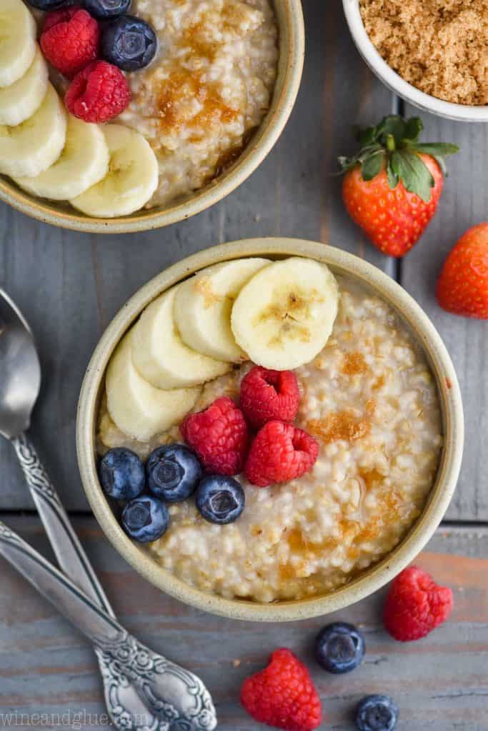 overhead view of two small bowls of instant pot steel cut oats with berries, banana slices, and brown sugar on a blue wood board