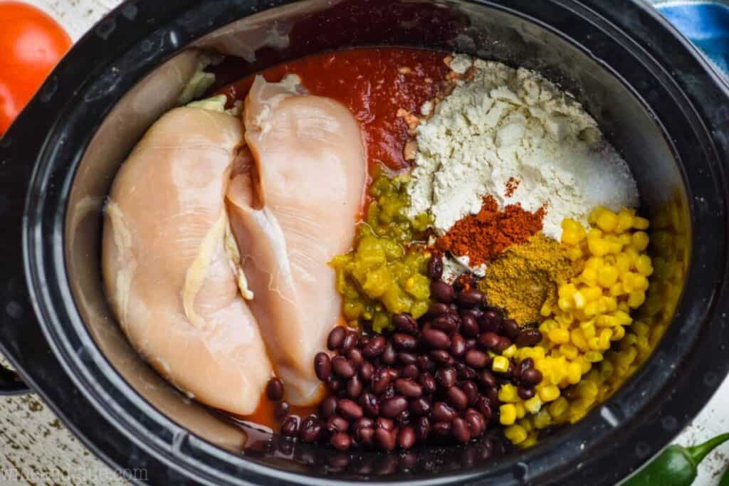 overhead photo of chicken black beans, corn, and spices in a crock pot to make enchilada soup