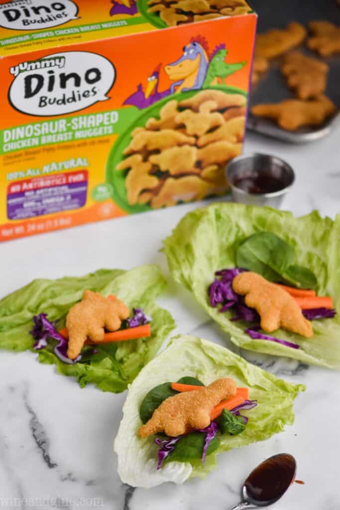 three lettuce wraps made with dinosaur chicken nuggets with a box of yummy Dino buddies in the background