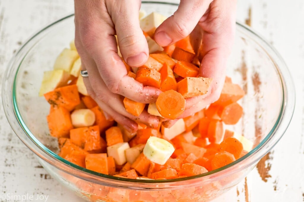 two hands tossing carrots, sweet potatoes, and parsnips that have been seasoned