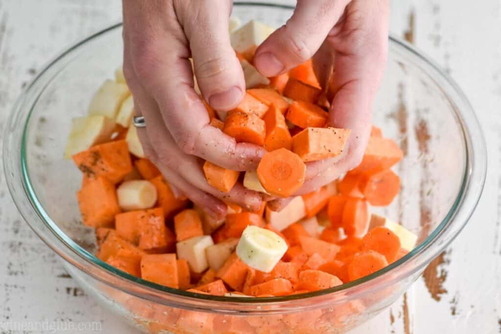 two hands tossing carrots, sweet potatoes, and parsnips that have been seasoned