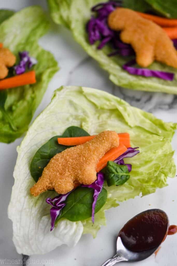 a lettuce wrap for kids made with dinosaur chicken nuggets, cabbage, spinach leaves, and carrot pieces all on a piece of iceberg lettuce