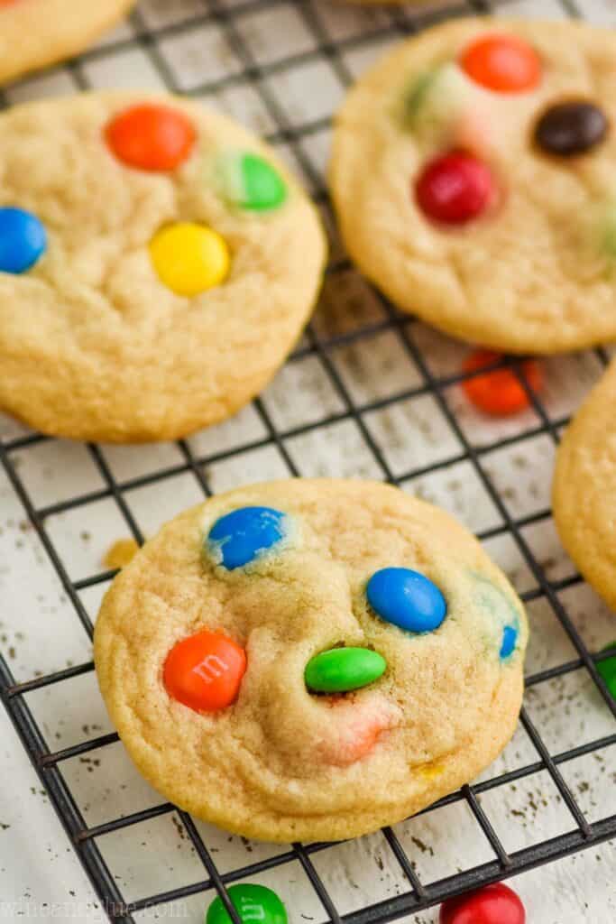 close up of an m m cookie on a wire cooling wrack with other cookies in the background