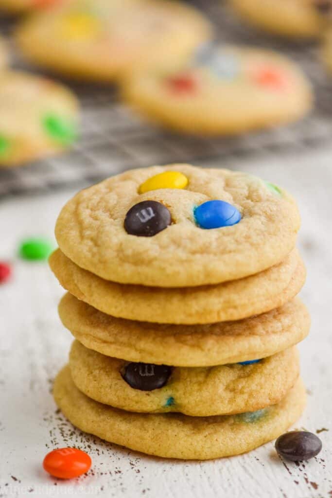 stack of five m n m cookies with more on a cooling rack in the background