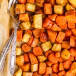 overhead view of a parchment lined baking sheet full of roasted root vegetables with a fork and spoon in the pan