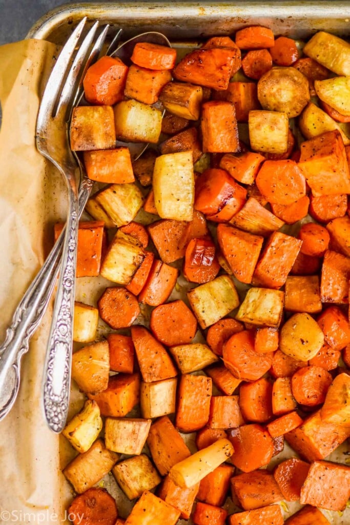 overhead view of a parchment lined baking sheet full of roasted root vegetables with a fork and spoon in the pan