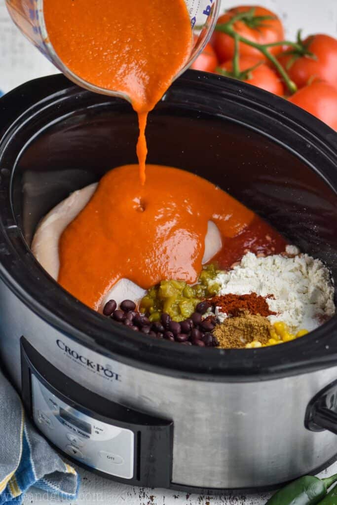 a crockpot with ingredients for enchilada soup and homemade enchilada sauce being poured into it