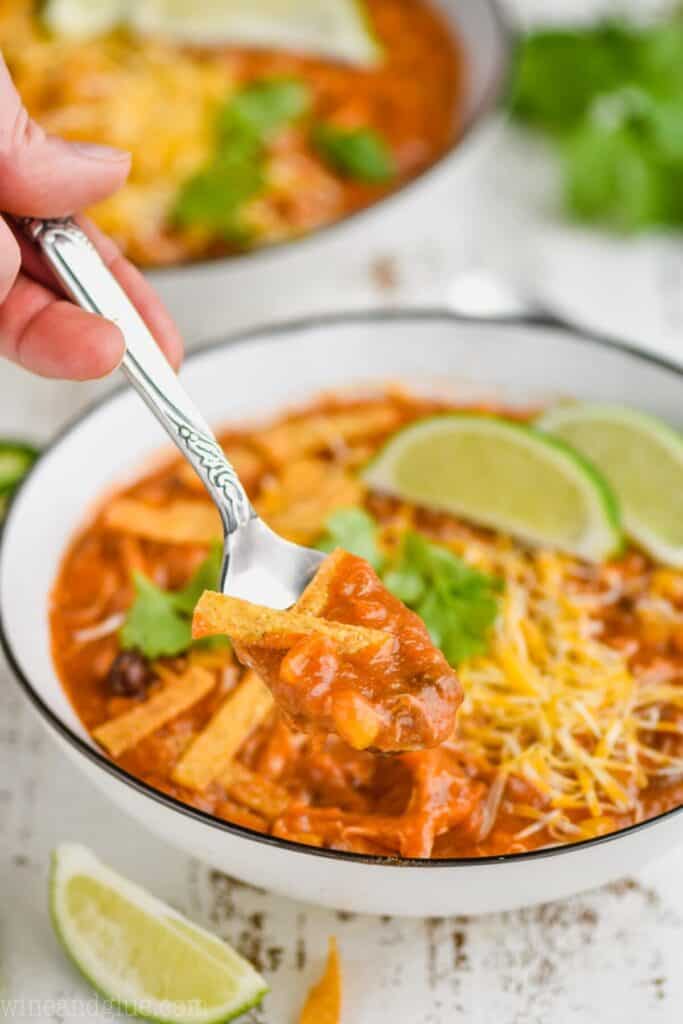 a small white bowl with a spoon dishing up chicken enchilada soup