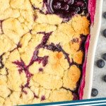 pinterest graphic of close up overhead overhead a serving spoon in a ceramic dish filled with blueberry cobbler, says: blueberry cobbler simplejoy.com