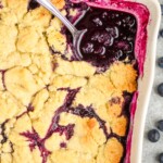 close up overhead overhead a serving spoon in a ceramic dish filled with blueberry cobbler