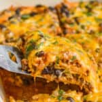 piece of cheese enchilada casserole being lifted out of baking dish