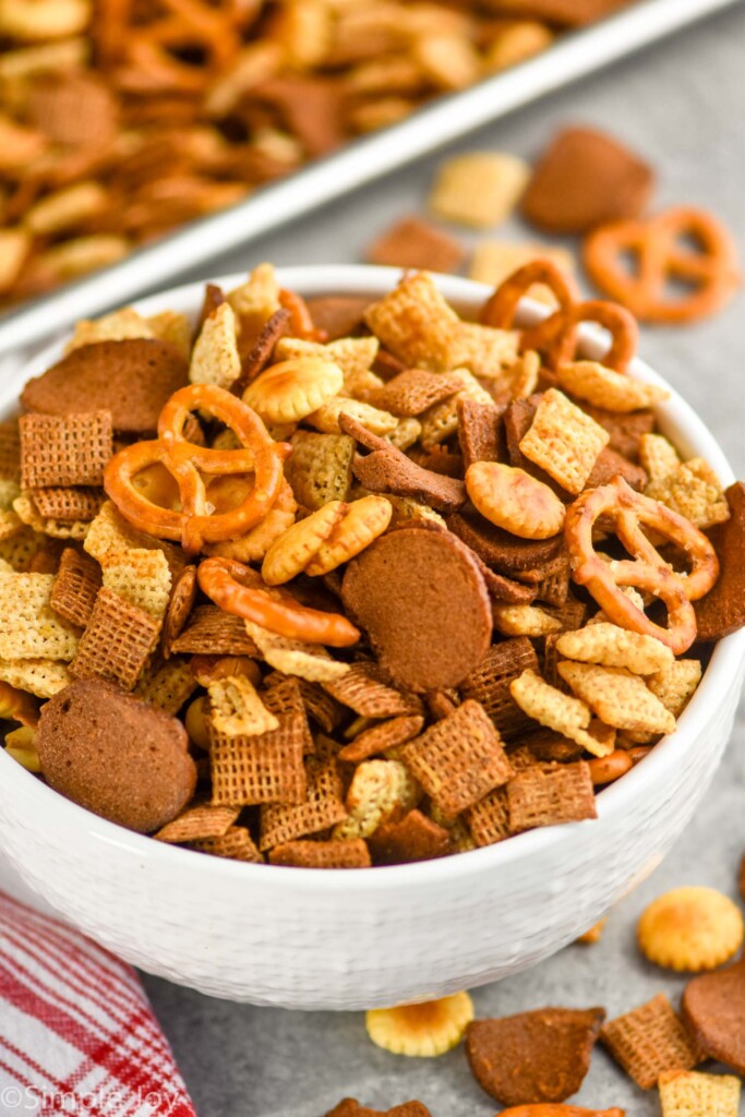 close up of a white bowl of Chex mix recipe with some around the bowl