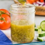 pinterest graphic of greek salad dressing being poured from a spoon into a jar, says: "greek dressing simplejoy.com"