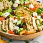 pinterest graphic of greek salad dressing being poured over a salad, says: "super easy greek dressing simplejoy.com"