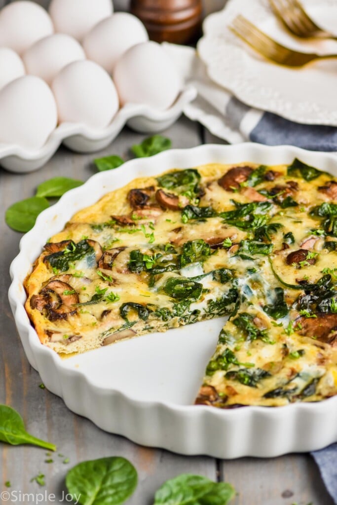 a spinach and mushroom quiche in a white quiche dish with a piece missing