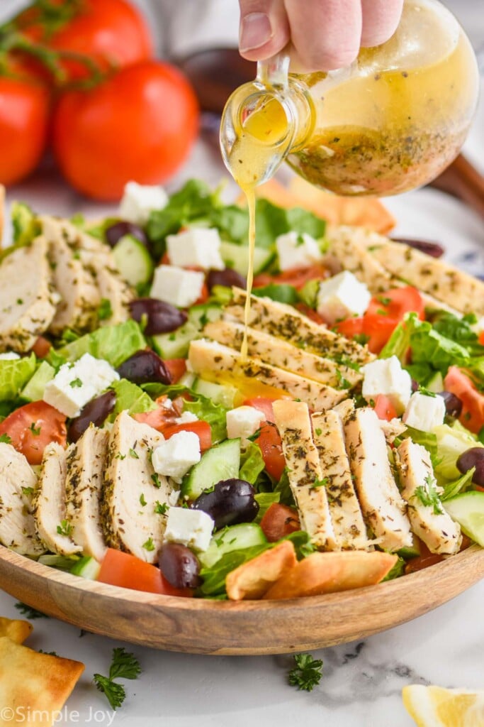 greek salad dressing being poured over a greek chicken salad