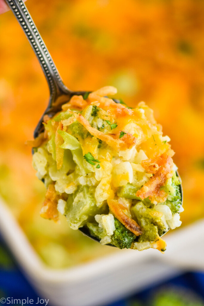 serving spoon holding chicken broccoli casserole with the rest of the casserole blurred in the background