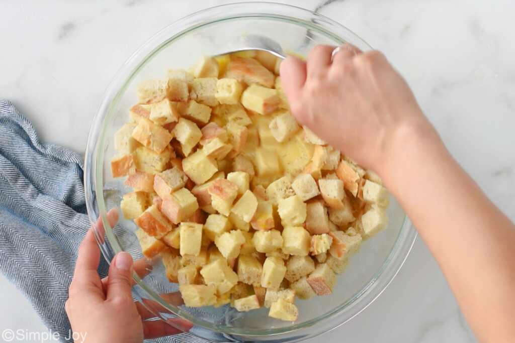 hands mixing bread with egg custard in a large bowl for French toast casserole