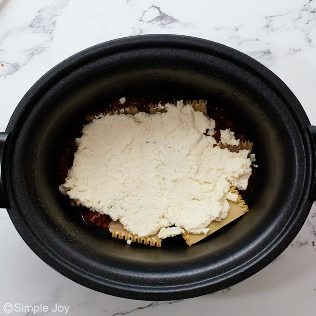 overhead of a crockpot with lasagna noodles, sauce, and cheese mixture