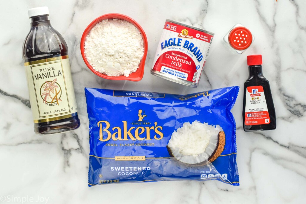 ingredients for coconut macaroons, vanilla extract, a measuring cup full of flour, sweetened condensed milk, a salt shaker, vanilla extract, and coconut shreds