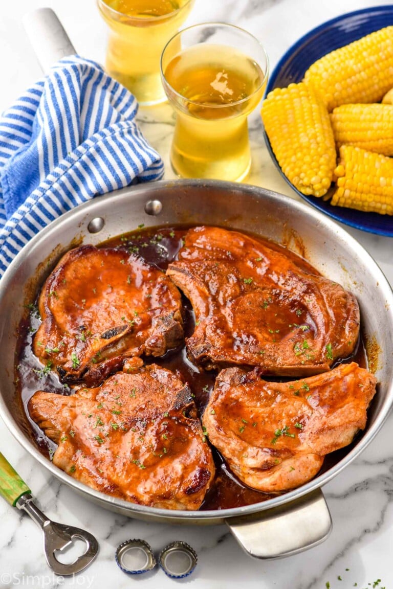 Overhead photo of BBQ Pork Chops in a skillet. Glasses of beer and corn on the cob beside skillet.