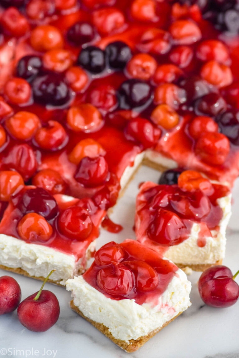 cherry cheesecake bars with two bars cut from pan, fresh cherries sitting beside