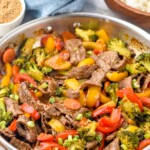 Pan of beef stir fry with bowl of white rice and bowl of seasoning sitting in background